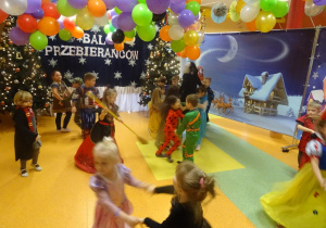 Dzieci tańczą w parach, jedna z dziewczynek tańczy z miotłą.